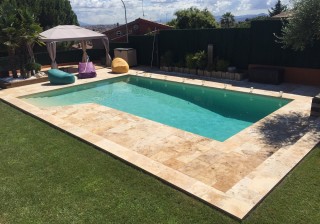 Piscina con playa y escaleras en travertino, jardineras y carpa